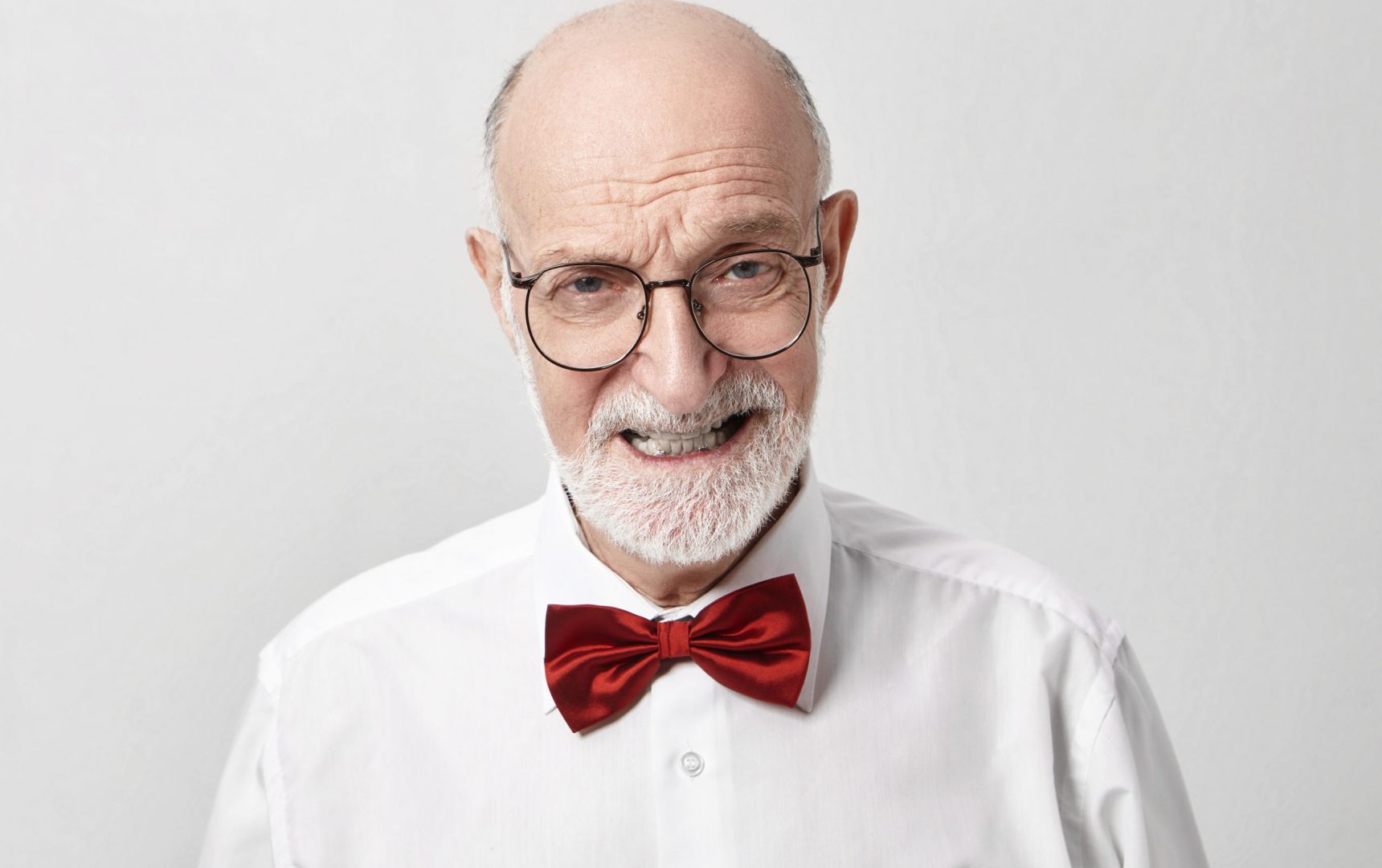 Negative human emotions, feelings and reaction. Picture of angry furious male pensioner with gray stubble clenching teeth mad at noisy naughty grandchildren posing in studio in stylish accessories